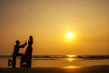 Romantic marriage proposal at the seaside at sunset on the beach sea. Young couple in love female said yes to offer of marriage February 14, St. Valentine's Day silhouette. copy space