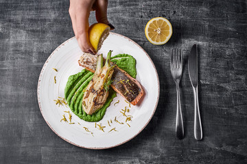 hand squeezes lemon over Baked salmon steak with mashed green peas , caramelized onions.