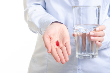 Red capsule pill and glass of water medicine in woman hand on white background, pharmacy concept
