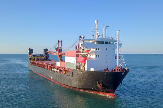 Large Cargo and RoRo (Roll On-Off) ship at sea, loaded with a small amount of shipping containers and two large cranes - Aerial image.
