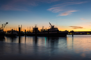 Fototapeta premium Sunset behind a silhouette of a resting shrimp boat with calm water