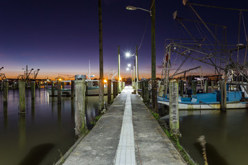 Obraz premium Stare zabytkowe doki były zmęczone krewetki czekają na pracę nad spokojną wodą o głębokim fioletowym i pomarańczowym zachodzie