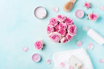 Aromatherapy, spa, beauty background with roses flowers, cosmetics and candles on blue table. Flat lay style.