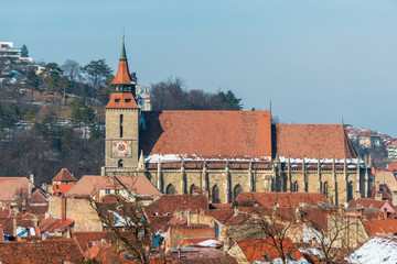 Fototapeta premium Medieval town cityscape with red tile roofs and a Gothic architectural style church in the background. Black Church rising over the city of Brasov, Transylvania, Romania.
