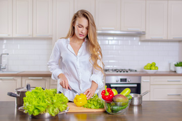 Obraz na płótnie Canvas Beautiful girl in a white shirt prepares vegetables in the kitchen