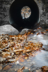 view through water tunnel tube in fall scenery in forest with flowing river in long exposure 