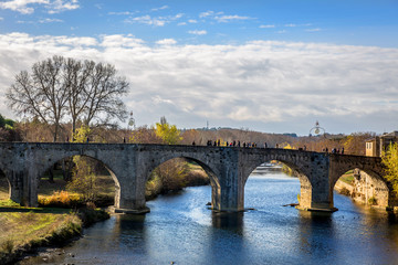 Fototapeta na wymiar Tourist and locals crossing a old stone bridge over a calm river in Carcassonne in France