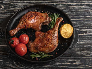 duck legs roasted juicy with with tomato and lemon in a frying pan , black surface, close up