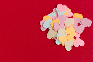 Many colorful paper heart shaped confetti on pink or red background. Valentine's concept card. Copy space