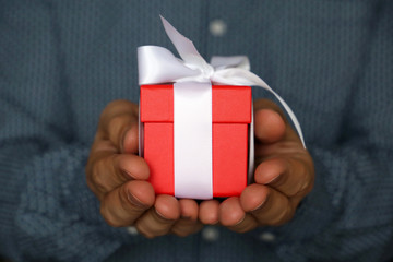 Gift box in hands close up. Man holding red gift box with white ribbon, present for birthday or Valentines day