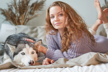 woman in a cozy knitted sweater relaxes on the bed. her dog is near. best friends concept