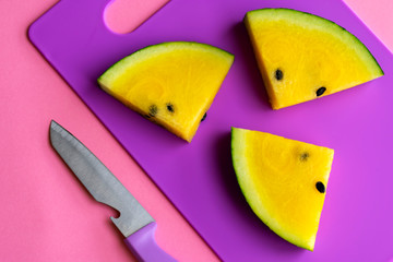 Ripe fresh slices of yellow watermelon on violet cutting board on pink background. Top view. Copy space.