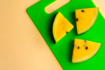 Ripe fresh slices of yellow watermelon on green cutting board on yellow background. Top view. Copy space.