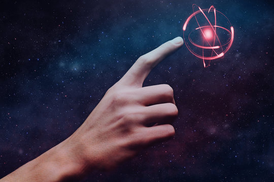 Human forefinger touches atom. Nebula dust  in infinite space. Mixed media.