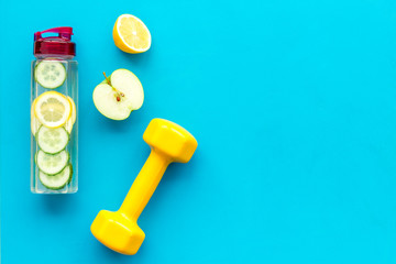 Healthy fruit water for sport, fitness. Bottle of water with lemon and cucumber near sport equipment dumbbells on blue background top view copy space