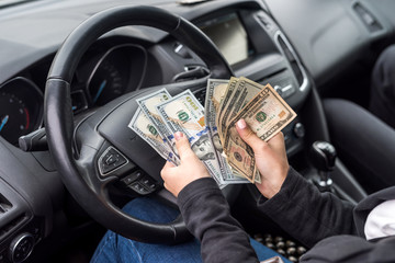 Female hands with dollar banknotes closeup on steering wheel