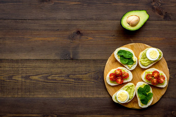 Fototapeta na wymiar Healthy snacks. Set of toasts with vegetables like avocado, guacamole, rocket, cherry tomatoes on dark wooden background top view copy space