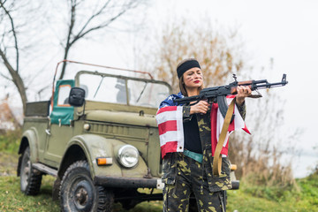 Woman with american flag and rifle near military car