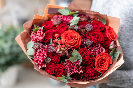 beautiful fresh cut bouquet of mixed flowers in woman hand. the work of the florist at a flower shop. Bright juicy red colors