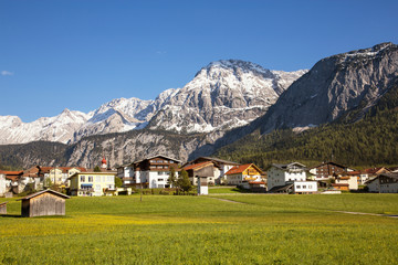 Fototapeta na wymiar View of the village of Ehrwald (Austria) and its beautiful surrounding mountains (Zugspitze Arena) and green alp meadows. Shot in afternoon sunlight.