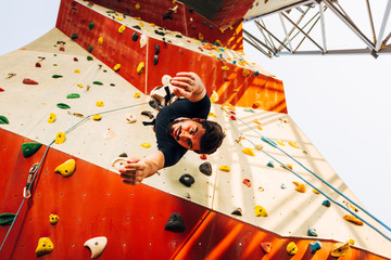 Young man descend of artificial rock wall at gym