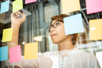 Young woman designer writing new ideas at sticky notes.