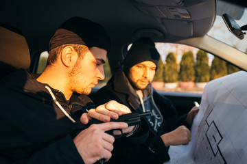 Two robbers planning and pointing on the blueprint(map) their objective while holding their guns.