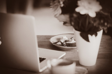 Notebook computer and plate with cake on a talbe in breakfast time. . Image in sepia color style