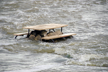 empty wooden picnic table on rocks in river flood