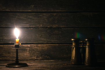 Binoculars and burning candle on the wooden table background with copy space. Travel or adventure...