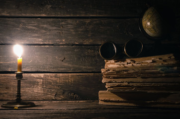 Binoculars, globe, stack of books and burning candle on the wooden table background with copy...