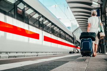 Frau auf dem Bahnsteig geht mit Gepäck den Zug entlang 