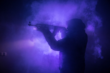 Fototapeta na wymiar Silhouette of man with assault rifle ready to attack on dark toned foggy background or dangerous bandit in black wearing balaclava and holding gun in hand. Shooting terrorist with weapon theme decor