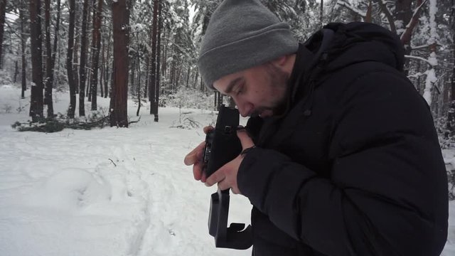 Photographer is standing in the deep snow in the winter forest and taking a shot on vintage medium format film camera. Side medium view