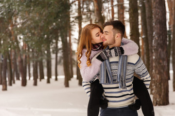Fototapeta premium Winter, couple in love. Young man and woman embracing in snowy forest. Romantic couple in winter wear enjoying snowfall. Love story in the winter forest