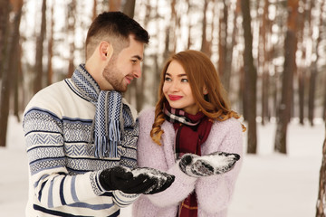 Winter, couple in love. Young man and woman in knitted wear holding white snow in hands. Romantic couple enjoying snowfall. Love story in cold day