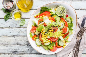 Healthy vegetable salad of fresh tomato, cucumber, lettuce and corn on plate, top view. Diet menu.