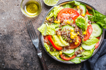 Fresh healthy salad with quinoa, red tomatoes, sweet pepper, cucumber, corn and avocado on stone background, top view. Healthy food. Superfood meal.
