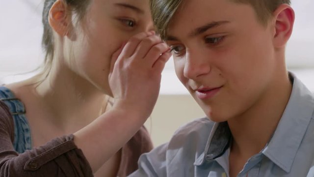 Tilt up close up shot of teenage boy playing wooden block game, his female friend whispering something funny to him, then both smiling