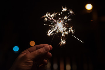 Burning sparkler in hand with blurred lights in the background