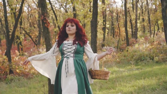 a pretty cute rural red-haired girl from a simple village dressed in national Bavarian clothes walks along the autumn lem with a basket, a magnificent model in a green dress and white loose shirt