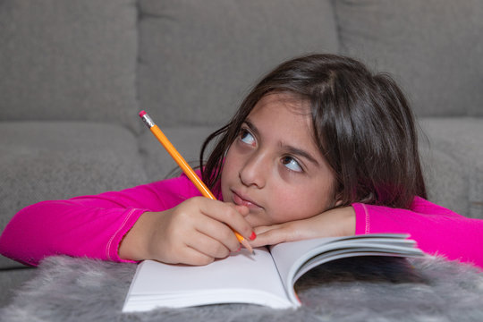 A young girl holding a yellow pencil is thinking while doing her homework