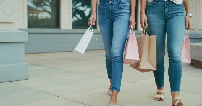 Young women in blue jeans shopping walking with shopping bags by storefront
