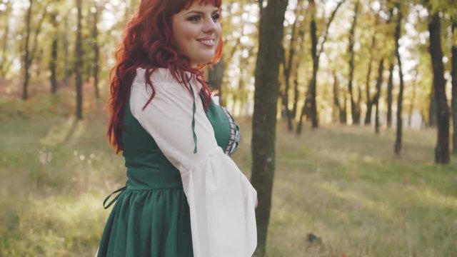 beautiful smiling big model with bright red hair in a national light simple dress in green and white color whirl in the autumn forest, pretty girl poses for the camera, image of a brave princess