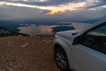 Fototapeta na wymiar white suv car at cliff sunrise over lake on background