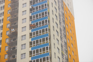 Concept of apartment building under construction close-up. Exterior of multicolor new multi-story residential building. Background with yellow walls, white plastic windows and blue loggias. Copy space