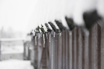 icicles hang and snow falls on the roof of a wooden house