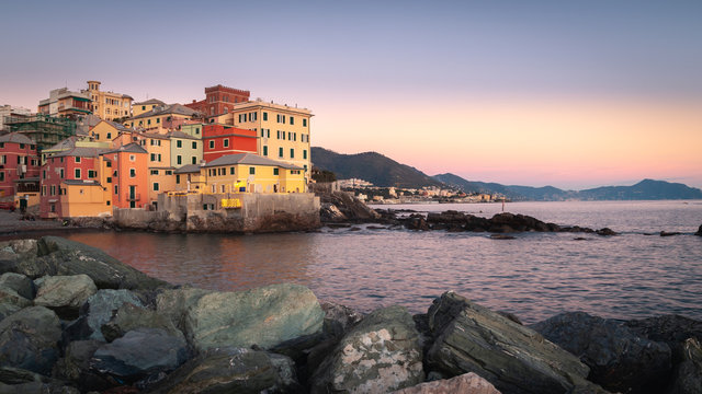 Genoa, Italy. Amazing panorama at sunset on the ancient fishing village of Boccadasse overlooking the sea. Rocks in the foreground. Background with Ligurian mountains and the promontory of Portofino