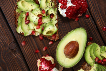 sliced avocado and ripe pomegranates on toast bread with spices and avocado.