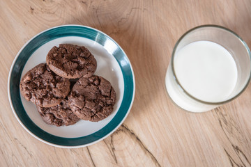 A cup of milk and plate of cookies of a brown desk